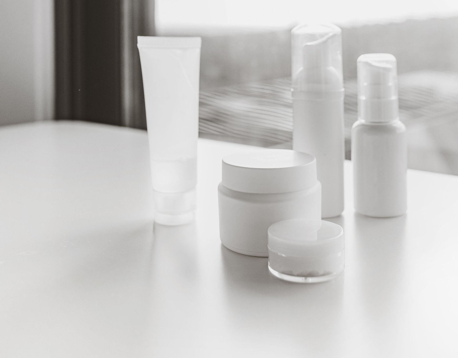 Plain, unlabelled cosmetic tubes, jars and pump bottles on a white table